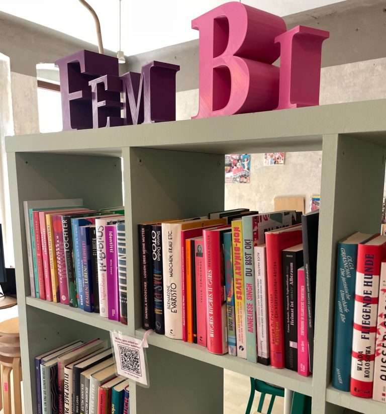 Bücherregal mit bunten Büchern und den Buchstaben "FEM Bi" oben drauf.