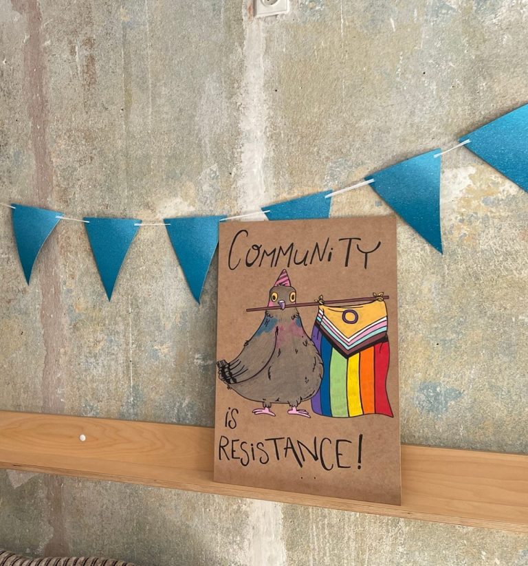 Ein einladender Raum mit bunten Dekorationen und dem Wort „QUEER“ an der Wand.